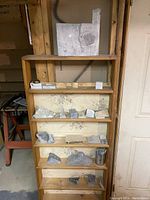 Wooden shelf with multiple shelves containing various stones and rocks, raw and partially shaped for carving.