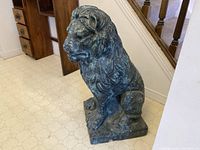 Side-angle view of a seated lion statue showing detailed mane and side body posture with faux bronze patina on concrete material.