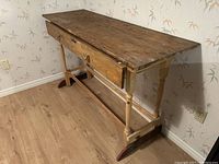 Farmhouse work table angled showing tabletop, drawer open, with brass knobs and stamped maker's mark.