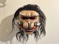 Front view of the Barong Rangda wooden mask showing carved face details and attached hair