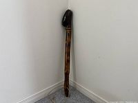 Full view of the handmade shillelagh walking cane standing upright against a wall, showing the length and carved wood pattern.