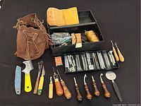Full view of leather tools including pouch, toolbox, assorted stamps, wooden handled tools, yellow raker, blue edge beveler, and thread.