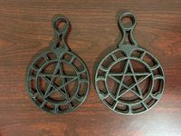 Pair of vintage Griswold cast iron trivets front view on wood surface, showing pentagram star and ring design with handles