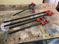 Four pipe clamps including three traditional cast iron pipe clamps and one quick-release clamp on a workbench