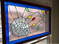 Stained glass window hung by chain in a window with spiderweb and colored leaf design with blue border.