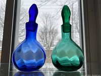 Two bottles with stoppers in place against window backlight showing cobalt blue and teal green glass with diamond pattern.