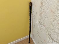 Full-length view of the walking stick showing knobby texture and natural shape leaning against a wall.
