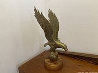 Front view of the brass eagle sculpture mounted on a wooden base, showing details of wings and head.