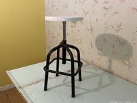 Front side view of the vintage industrial adjustable stool showing the white wooden seat and black metal base with footrest.