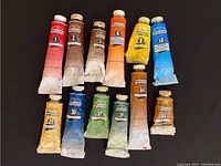 Full set of 12 Windsor & Newton Winton Oil Colour paint tubes laid out on dark surface showing wear and various colour labels.