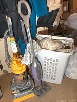 Dyson vacuum and Shark floor steamer standing upright next to a laundry basket and clothing.