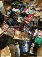 Overview of men's clothing, graphic tees, pants, shorts, and accessories spread on the floor.
