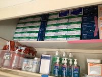 Photo showing boxes of Curad disposable gloves, FitGuard Touch gloves, disinfectant sprays, and antiseptic bottles arranged on a shelf and in plastic containers