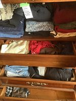 Drawer containing folded men's heavy knit sweaters in navy, grey with pattern, red, cream, and scarves in red, green, and brown.