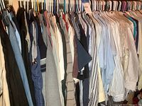 Photo showing wide assortment of men's shirts, mostly dress and casual golf style, hung on hangers in a closet, various colors and patterns.