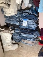 Closet floor view with multiple stacks of folded jeans, one white snow boot, and corner of cushions.