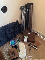 Full view of all lot items arranged on floor including tote bag, metal poster tube, camera, tripods, golf accessories.