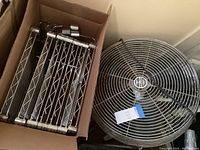 Top-down photo showing several metal bars with wire grid design inside a cardboard box alongside the industrial fan on the floor.