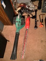 Photo showing green gas blower, red hedge trimmer, black portable puller, and coiled cables.