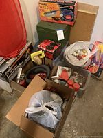 Overall lot showing welding kit box on top of a green metal toolbox, Craftsman sander box below, bag of golf balls and tees in white plastic bag, chemical bottles with red caps, and assorted tools like a screwdriver and scraper.