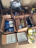 Wide view showing multiple boxes with various hardware items, cable ties, masks, tiedowns, and two boxed white bathroom utility fans on floor