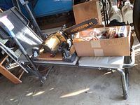 Metal weight bench with chain saw and box of tools on top, side view