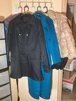 Four women's coats hanging on a rack: black wool blend coat, teal wool coat, cream/light brown faux fur jacket, and black leather bomber jacket.