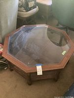 Octagonal coffee table made of wood and glass with glass inset top. Shows wood lattice lower shelf and carved legs.