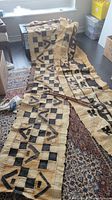 Photo showing both wall hangings unrolled on the floor with bamboo rods on top, showcasing geometric and tribal black patterns on natural beige fabric.