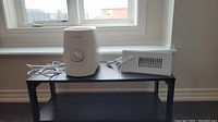 Side-by-side view of white Honeywell dehumidifier and white metal heat booster sitting on black surface near window.