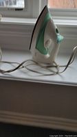 Philips iron side view showing white and mint green plastic with attached power cord, placed on windowsill.