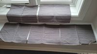 Five grey placemats arranged side by side and slid partially under two more grey placemats folded in half on a white surface by a window.