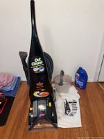 Full view of Bissell ProHeat carpet cleaner upright, cleaning fluids bottle, detachable fluid tank, and user manual on floor.