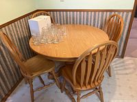View of round wooden kitchen table with four matching wooden spindle back chairs around it, glasses on table removed from sale.