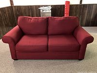 Front view of red fabric love seat showing two seat cushions and two attached back cushions with rolled arms.