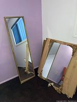 Full view of both mirrors side by side leaning against the wall, one full length with damage at bottom, one square with ornate corners