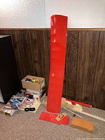 Photo of red model airplane wing about 36 inches in wingspan with assorted supplies and parts in cardboard boxes on carpeted floor.