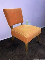 Front angle view of orange fabric upholstered wooden chair showing seat and backrest with wood legs and brass foot caps.