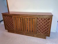 Front view of vintage wooden record player and radio cabinet with lattice speaker covers and spindle detail doors.
