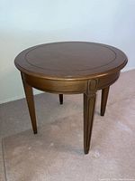 Full side view of the round wooden table showing four tapered legs and smooth surface finish.