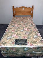 Full view of the single/twin sized bed including mattress, boxspring, and headboard against a white wall and dark carpet floor