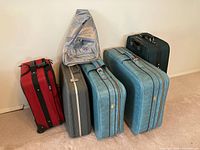 Photo showing all five suitcases and one shoulder bag arranged against a wall.