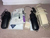 Photo showing three corded telephones and one answering machine with cords and instructions on carpet floor.