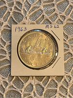 Reverse side of the 1963 Canadian Silver Dollar showing a canoe scene with two paddlers and a fur trader, with inscriptions and grade MS62 notation on the holder.