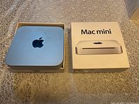 Top view of Apple Mac Mini A1347 computer in original box alongside the box lid with Mac Mini branding.
