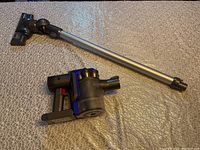 Dyson DC35 vacuum parts laid out showing main handheld unit detached from metal wand and brush head attachment.