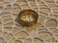 Gold colored men's ring resting on a patterned gold and white surface, showing side angle with stone accents visible.