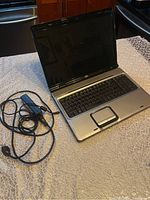 Full open view of HP Pavilion DV9000 laptop on a table with power adapter and cable beside it.