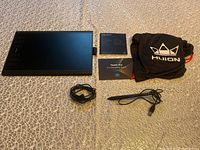 Photo shows the Huion digital art tablet, the digital pen with USB cable, USB cable for the tablet, quick start guide, thank you card, and Huion branded carry bag laid out on a textured surface.