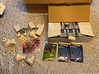 Photo showing multiple loose white bulb sockets/adapters, various smaller bulb packages, and a partially open box filled with Standard brand boxed light bulbs.